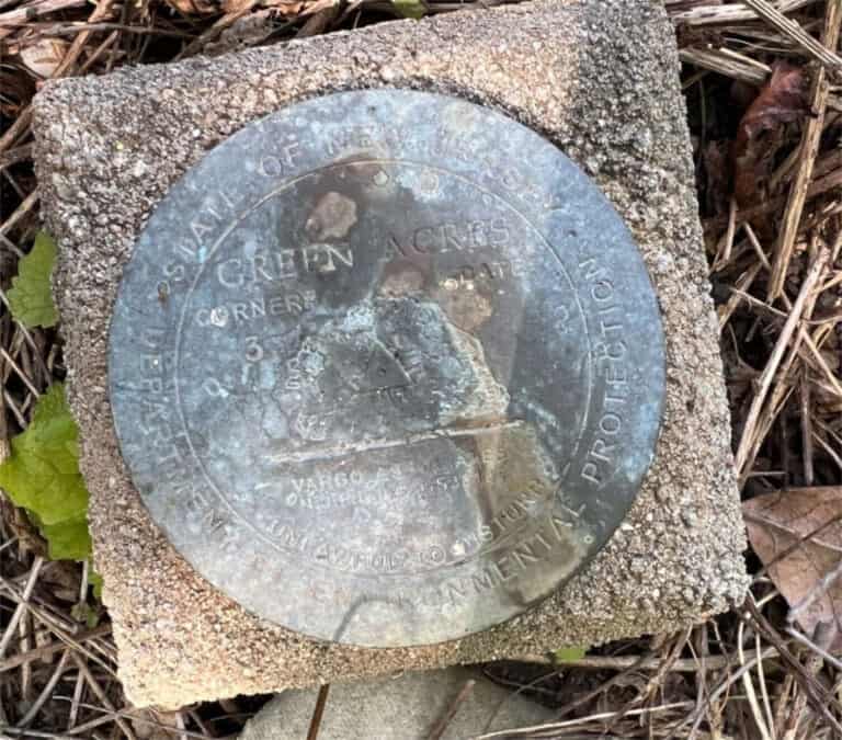 Old survey marker for Green Acres, located on the ground among leaves and soil.