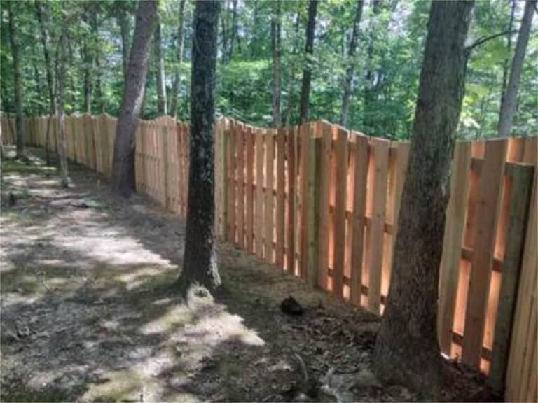 Custom wooden fence installed along a wooded area for privacy and security.